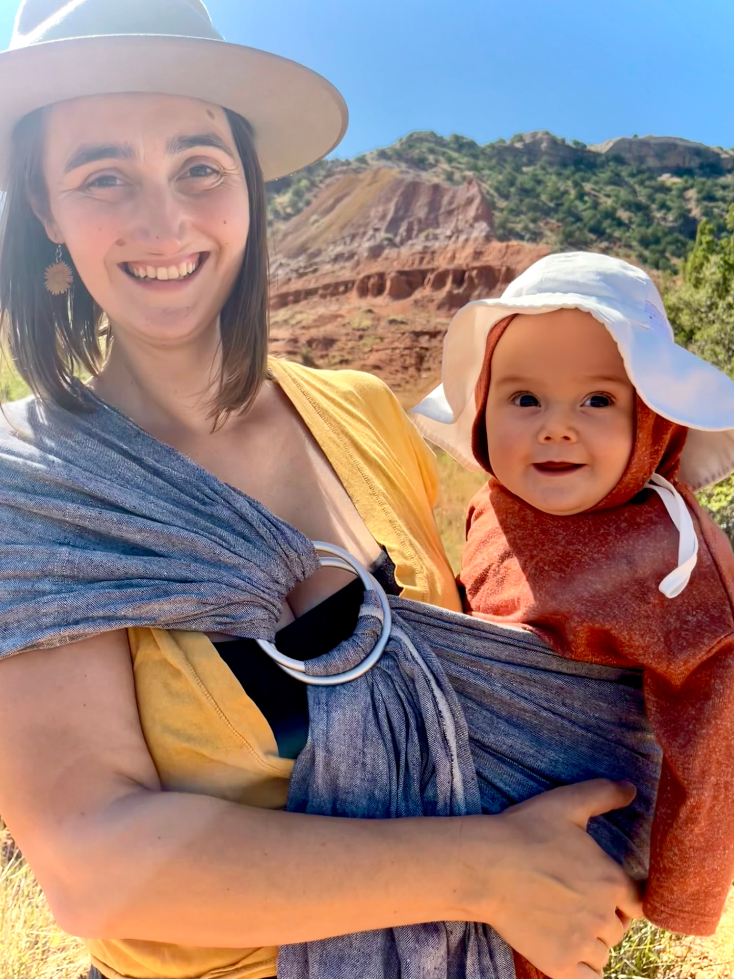 Nora Lisette smiling with her baby in a ring sling on a canyon trail