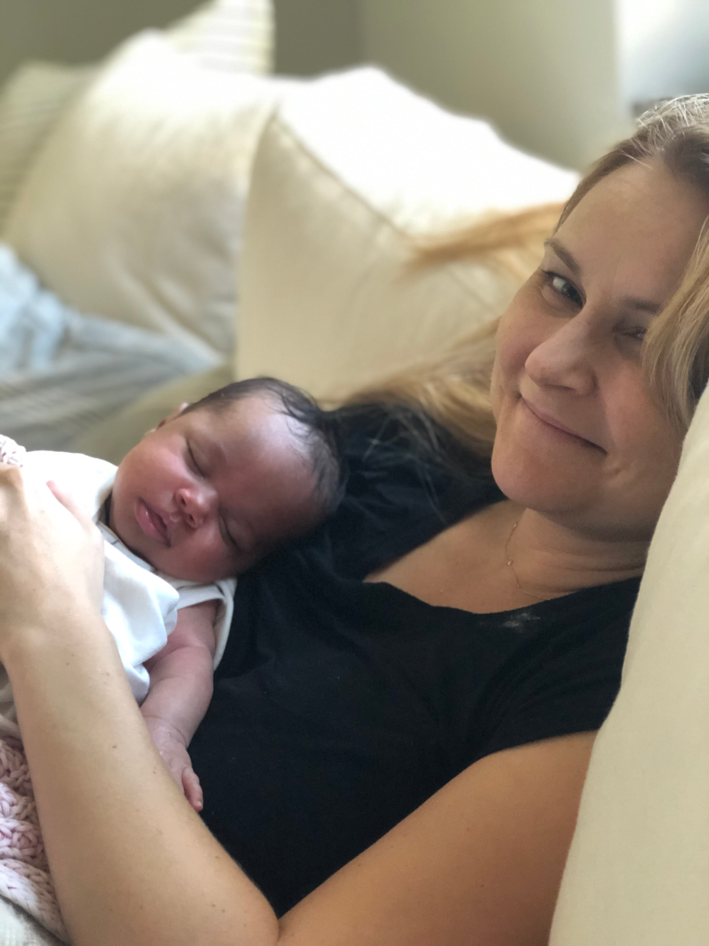 Nora lying on a couch smiling at her sleeping newborn